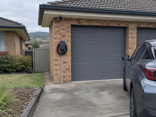 Wall-mounted EV charger beside a garage roller door on a brick home in Aberglasslyn