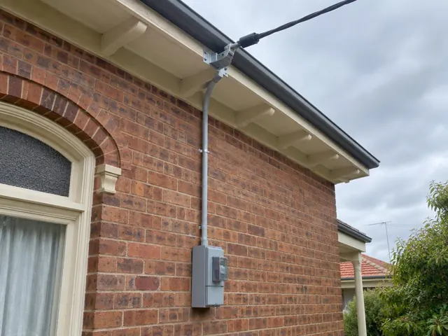 Overhead service cable and point-of-attachment bracket on a brick house wall in Maitland